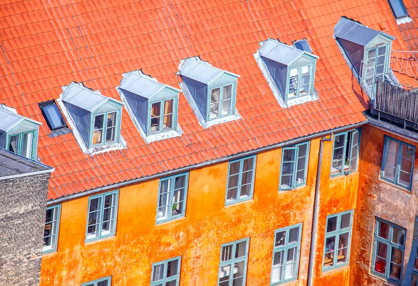 Orange etageejendom med rødt tegltag og en række tagkviste, set skråt oppefra