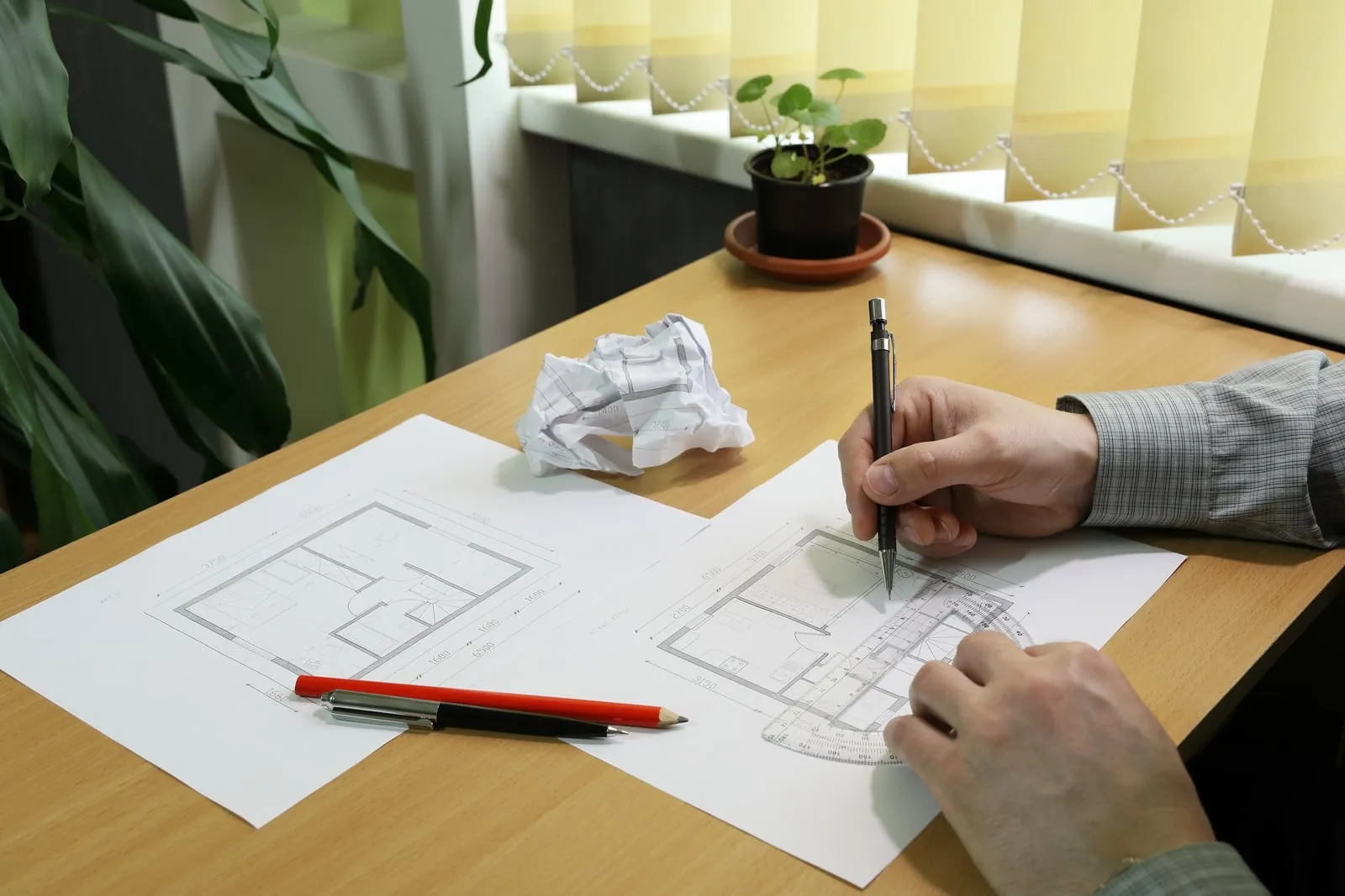 En person tegner med blyant på en plantegning ved et skrivebord